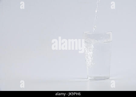 Verser de l'eau dans le verre clair sur fond blanc Banque D'Images