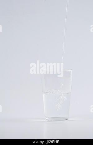 Verser de l'eau dans le verre clair sur fond blanc Banque D'Images