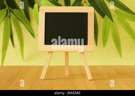 Vide petit tableau noir à écrire un message posé sur un chevalet sur un sol en bois avec un fond de feuillage vert Banque D'Images