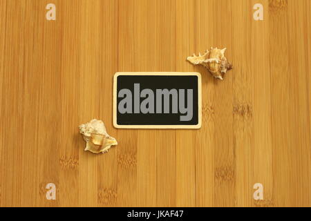 Petite ardoise vide de largeur pour écrire un message posé sur le sol brun bambou avec plage coquillages sur les côtés Banque D'Images