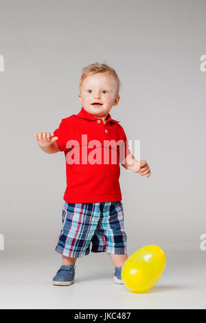 Bébé garçon debout sur le plancher avec un ballon jaune Banque D'Images