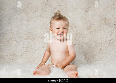 Crying baby boy dans les couches, assis sur une couverture maison laine shaggy Banque D'Images