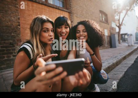 Femme amis assis à l'extérieur et faire des selfies téléphone intelligent. Multi Ethnic groupe de femmes de traîner dans la ville et taking self portrait avec Banque D'Images