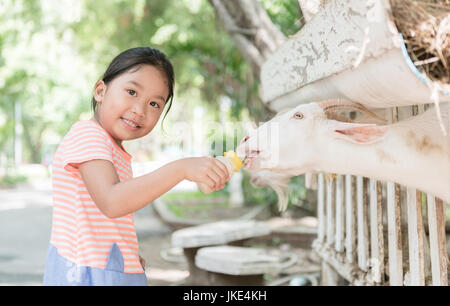 Cute farmer girl nourrir bébé avec bouteille de lait de chèvre d'élevage concept. Banque D'Images