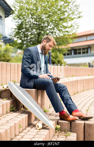 Businessman with skateboard using tablet et écouteurs Banque D'Images