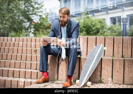 Businessman with skateboard using tablet et écouteurs Banque D'Images