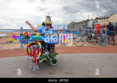 Utilisateur de fauteuil roulant à Morecambe, Lancashire, UK 23 Juillet, 2017. Mobilité Damon Vardon voyageant en fauteuil roulant motorisé un instrumentiste sur front de Morecambe. Les bandes d'un seul homme de tout le pays effectuée sur la promenade de Morecambe pour un festival de musique libre encore de mayhem et de divertissement. Banque D'Images