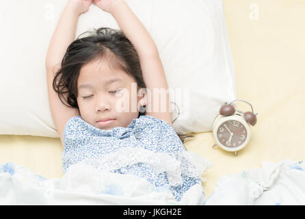 Cute girl dormir sur le lit avec réveil au matin. Banque D'Images