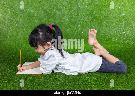 Chinois asiatique petite fille couchée sur l'herbe et écrit à l'extérieur parc Banque D'Images