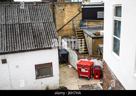 Ruelle urbaine avec bacs wheely rouge en mauvais état et les bâtiments de brique avec pas de personnes Banque D'Images