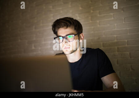 Vue rapprochée du jeune homme barbu à lunettes travaillant au bureau la nuit man using laptop Banque D'Images