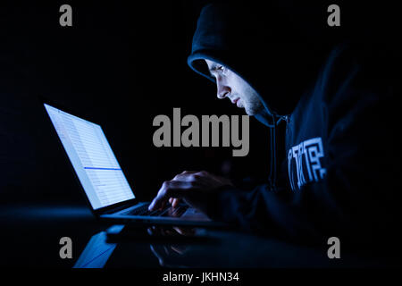 L'homme à un travail de capot à l'avant d'un ordinateur portable les programmes de craquage de hacker dans la nuit. Hacker Banque D'Images
