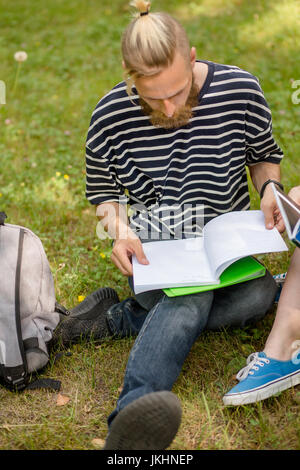 Garçon assis sur l'herbe d'étudiant d'étudier. Banque D'Images