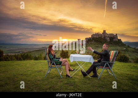 Couple in love boire du vin rouge dans la nature sous les ruines d'un château au coucher du soleil. Petit ami trows une tulipe à sa petite amie. Banque D'Images