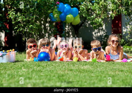 Groupe d'enfants dans des lunettes de soleil sur l'herbe en été. Banque D'Images