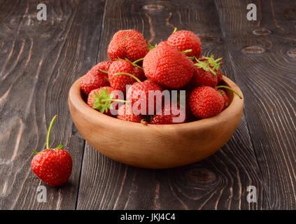 Une fraise mûre dans bol en bois et feuilles vertes sur l'ancienne table, vue du dessus Banque D'Images