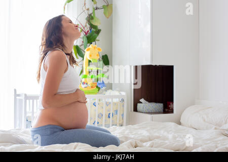 Belle Jeune femme enceinte, dans la douleur avec la contraction du travail, assis sur le lit dans la chambre, prepraring pour donner une naissance Banque D'Images