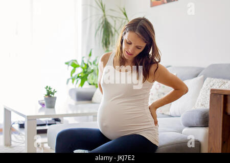 Jeune femme enceinte, avoir contraction douloureuse, en commençant le travail, assis sur le canapé Banque D'Images