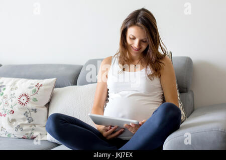 Jeune femme enceinte, avoir contraction douloureuse, en commençant le travail, assis sur le canapé Banque D'Images