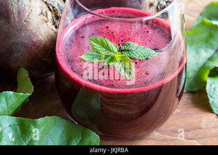 Le jus de betterave rouge dans un verre sur un fond de bois avec du citron et des feuilles de betteraves Banque D'Images