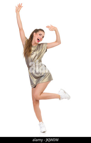 Happy young woman in robe or et blanc chaussures de danse sur une jambe, des cris et des armes légères, pleine longueur portrait isolé sur blanc. Banque D'Images