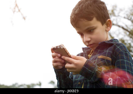 Un jeune garçon à l'extérieur jouer Pokemon rendez sur un téléphone intelligent. Banque D'Images