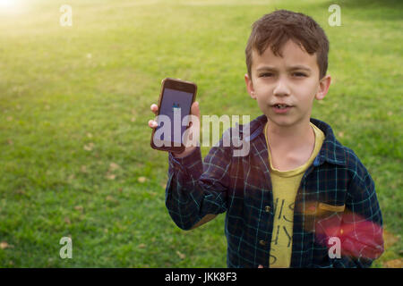 Un jeune garçon à l'extérieur jouer Pokemon rendez sur un téléphone intelligent. Banque D'Images