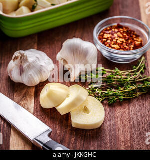 Ingrédients pour la préparation de l'ail rôti au thym frais, comprend et piment rouge broyé. L'ail haché dans un plat de cuisson en céramique. Couteau et roasti Banque D'Images