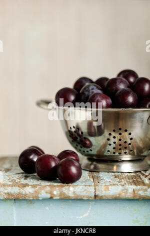 Les prunes mûres dans une passoire sur un fond de bois. Focus sélectif. Banque D'Images