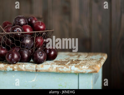 Les prunes mûres dans un panier sur un fond de bois. Focus sélectif. Banque D'Images