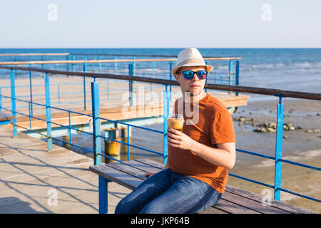 Portrait of cheerful attractive hipster barbu jeune homme boire un café glacé ou frappe sur l'arrière-plan de la mer Banque D'Images