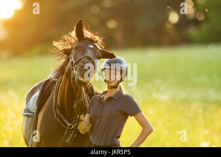 Jeune femme cavalier avec son cheval en bonne humeur en soirée coucher du soleil la lumière. La photographie style de vie en plein air Banque D'Images