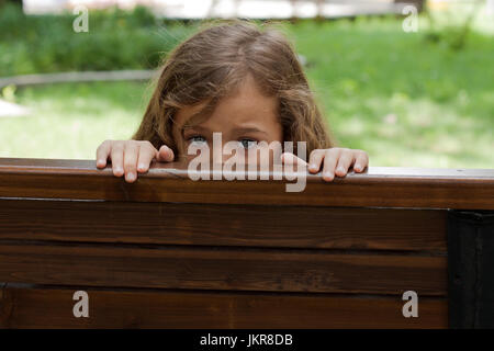 Kid se cacher derrière un BenchIn. Petite fille de six ans se cacher derrière un banc en bois dans le parc de l'été. Banque D'Images