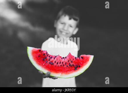 Little Boy holding tranche de melon d'outdoor, profondeur de champ, de couleur noir et blanc sélectif Banque D'Images