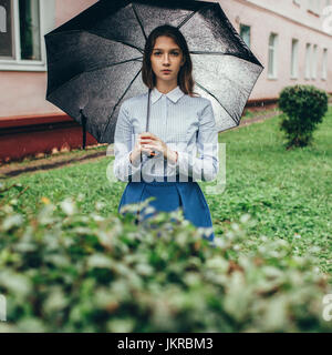 Portrait d'adolescent holding umbrella en se tenant sur le terrain herbeux pendant la pluie Banque D'Images