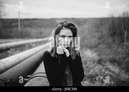 Portrait of teenage girl with hands clasped debout par des tuyaux sur terrain against sky Banque D'Images