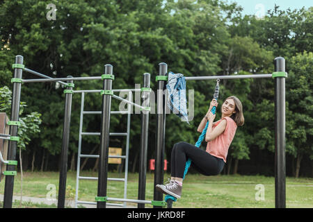 Full Length portrait of smiling young woman hanging de jungle gym corde au park Banque D'Images