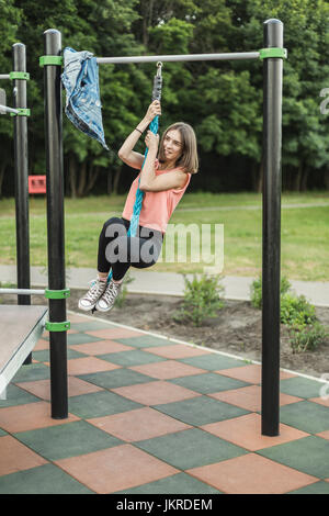 Happy young woman hanging de corde de jungle gym at park Banque D'Images