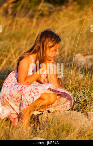 Enfant fille dans une robe sur une prairie rocheuse au coucher du soleil Banque D'Images