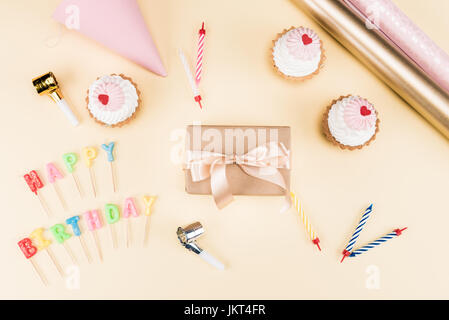 Vue de dessus de joyeux anniversaire lettrage, enveloppe avec ruban, gâteaux et cartes colorées sur rose, anniversaire concept Banque D'Images