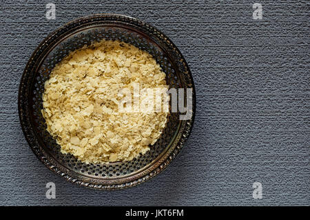 Vue de dessus de flocons de levure alimentaire séché sur une plaque de métal vintage sur un fond texturé, gris Banque D'Images