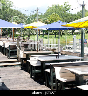 Vue d'un restaurant en plein air sur le front de mer. Il y a des sièges couverts de table de pique-nique en bois en bleu et jaune de parasols. Banque D'Images
