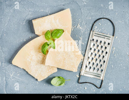 Coupe de fromage Parmesan avec râpe métallique et de basilic frais sur fond texturé en béton Banque D'Images