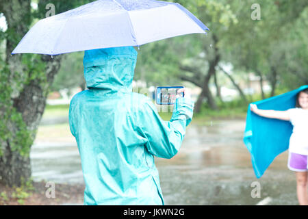 Femme prend une photo avec un smartphone d'une fille qui marche sous la pluie avec un parapluie. Banque D'Images