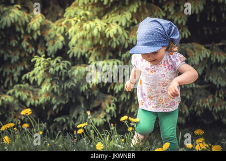 L'insouciance de l'enfance joyeuse ludique enfant fille courir sur prairie parmi les arbres et les fleurs pendant les vacances Banque D'Images