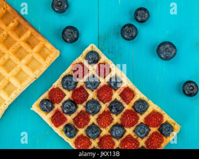 Les framboises et les bleuets sur une gaufre grillée against a blue background Banque D'Images