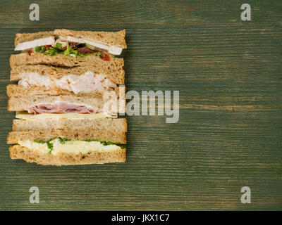 Sélection d'un assortiment de sandwichs dans du pain brun contre un fond de bois vert Banque D'Images