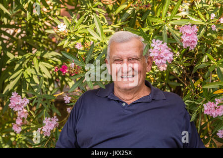 Portrait of smiling senior sur fond de lauriers-roses fleurs et plantes dans le jardin d'accueil Banque D'Images