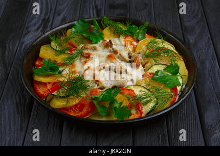 La viande avec du fromage et des tranches de pommes de terre, tomates et courgettes cuites au four dans la poêle en fonte Banque D'Images