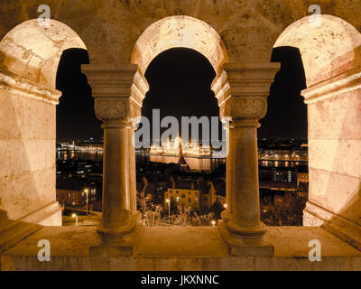 Vue nocturne de la célèbre parlement hongrois à travers le Danube à Budapest, vue à travers les arcades du château de Buda bastion des pêcheurs. Banque D'Images